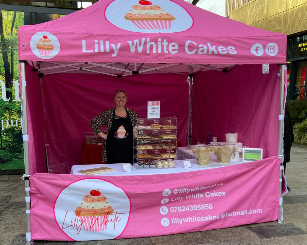 Pink 'Lilly White Cakes' tent with a woman standing behind it outdoors.